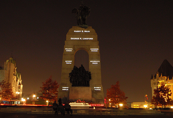 A small group gathers in front of the National War Memorial in Ottawa, one of six locations across Canada where the names of war dead are being projected